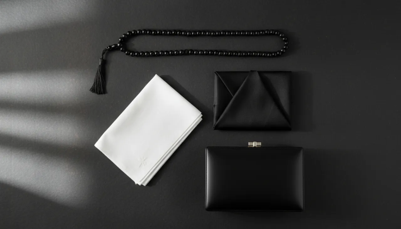 黒い数珠と白いハンカチ、黒い袱紗、フォーマルバッグが和紙の上に静かに並べられた俯瞰の静物